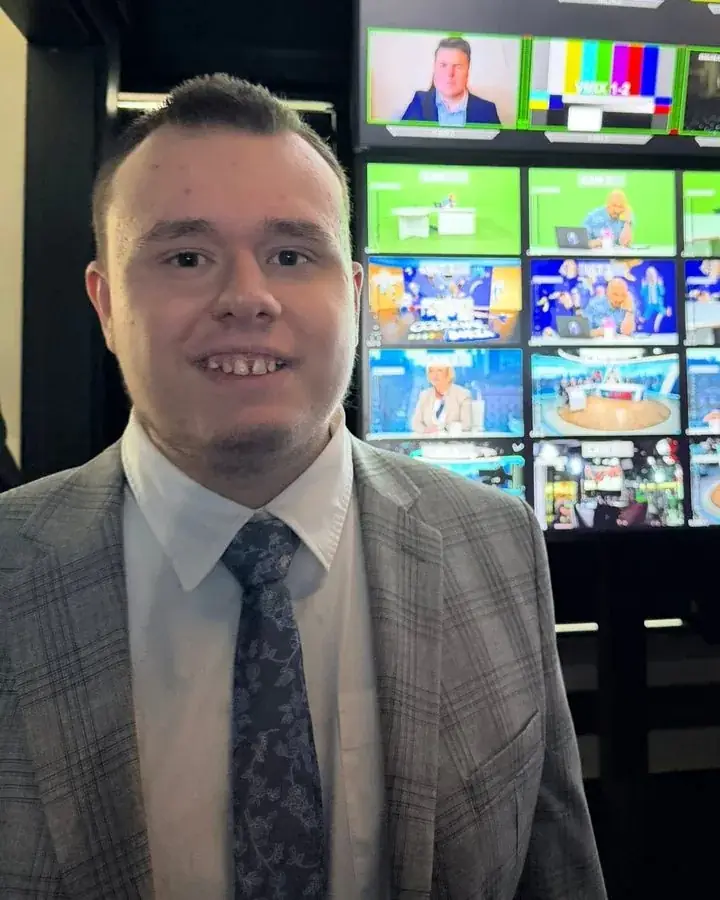 Marcin Jabłoński w marynarce na tle ściany monitorów reżyserki telewizyjnej